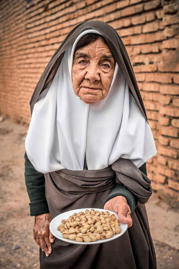 My Humble Welcome Portrait of an elderly woman offering pistachios as a welcome gift Buy Print